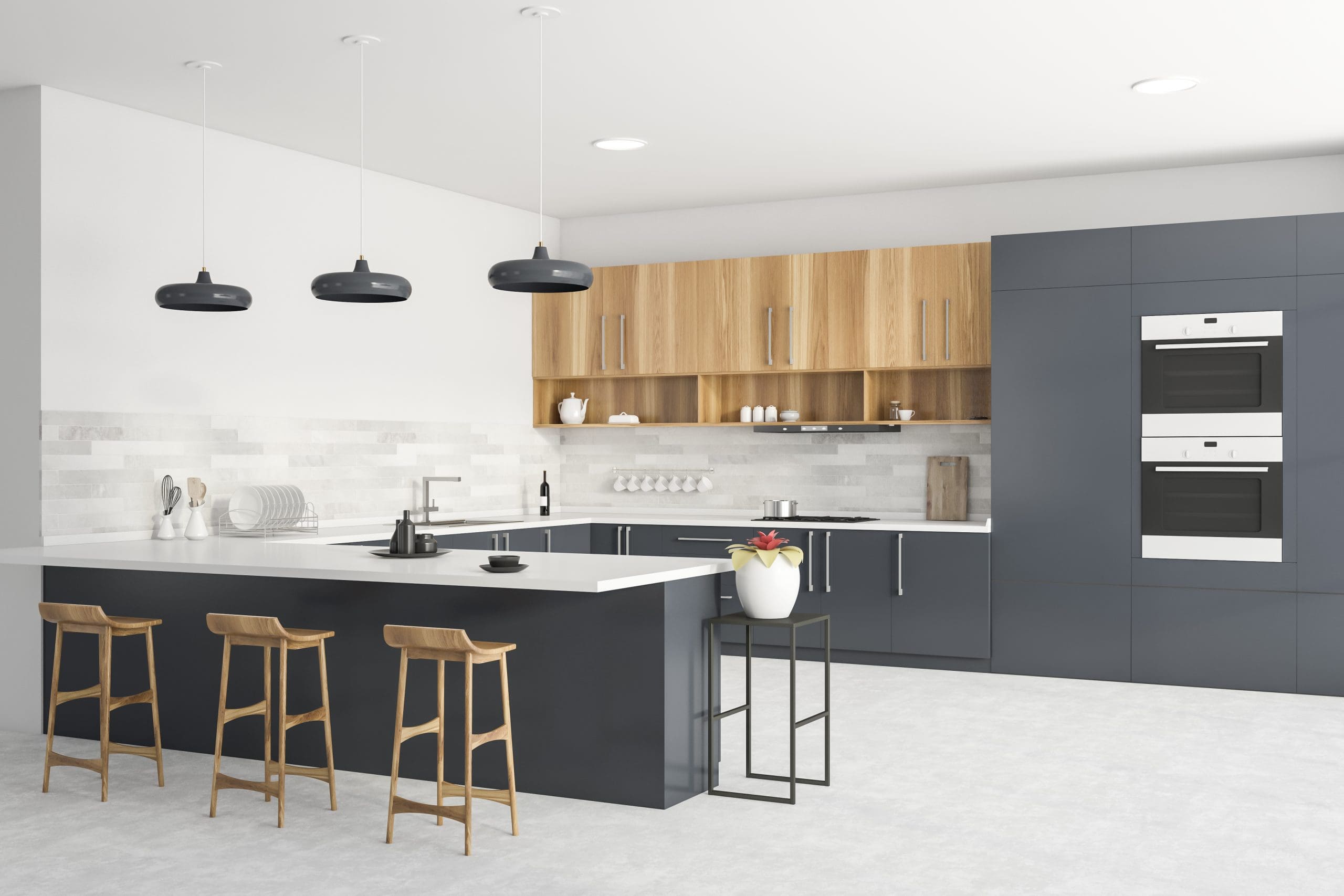 Modern kitchen featuring a large island with three wooden stools, black pendant lights, sleek grey cabinetry, and light wooden upper cabinets. The kitchen also has white countertops, a double wall oven, and a small table with a potted plant.