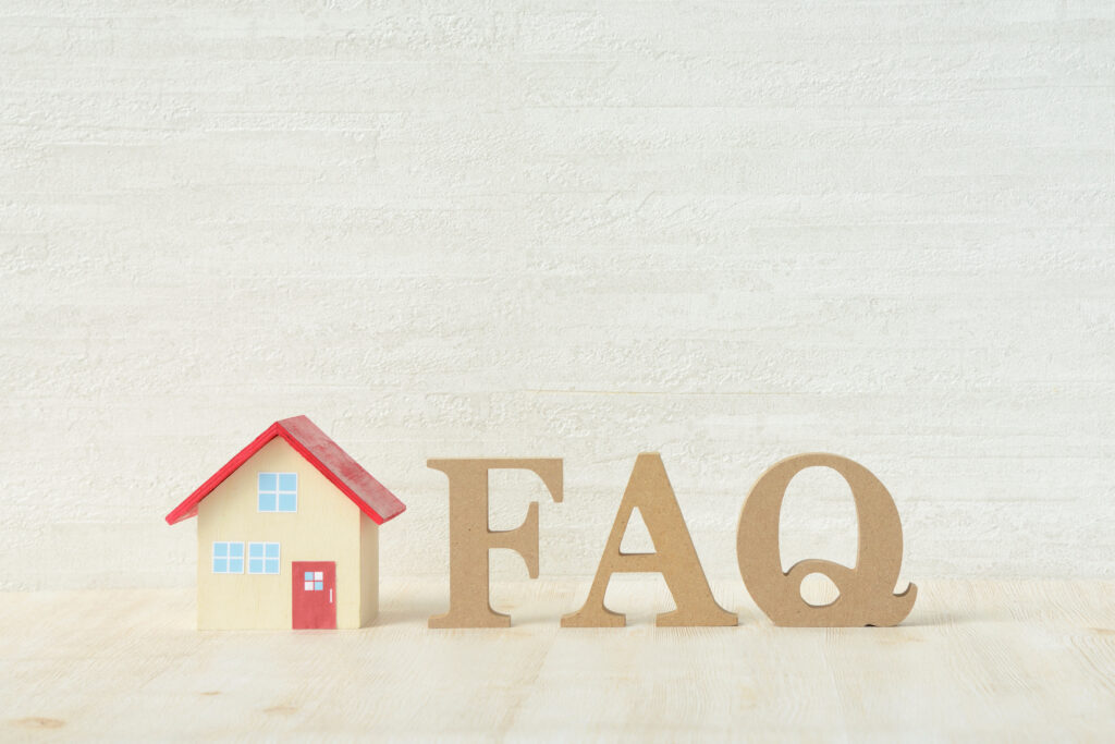 A small wooden house with a red roof stands next to large cardboard letters spelling "FAQ" on a light wooden surface against a pale textured background.