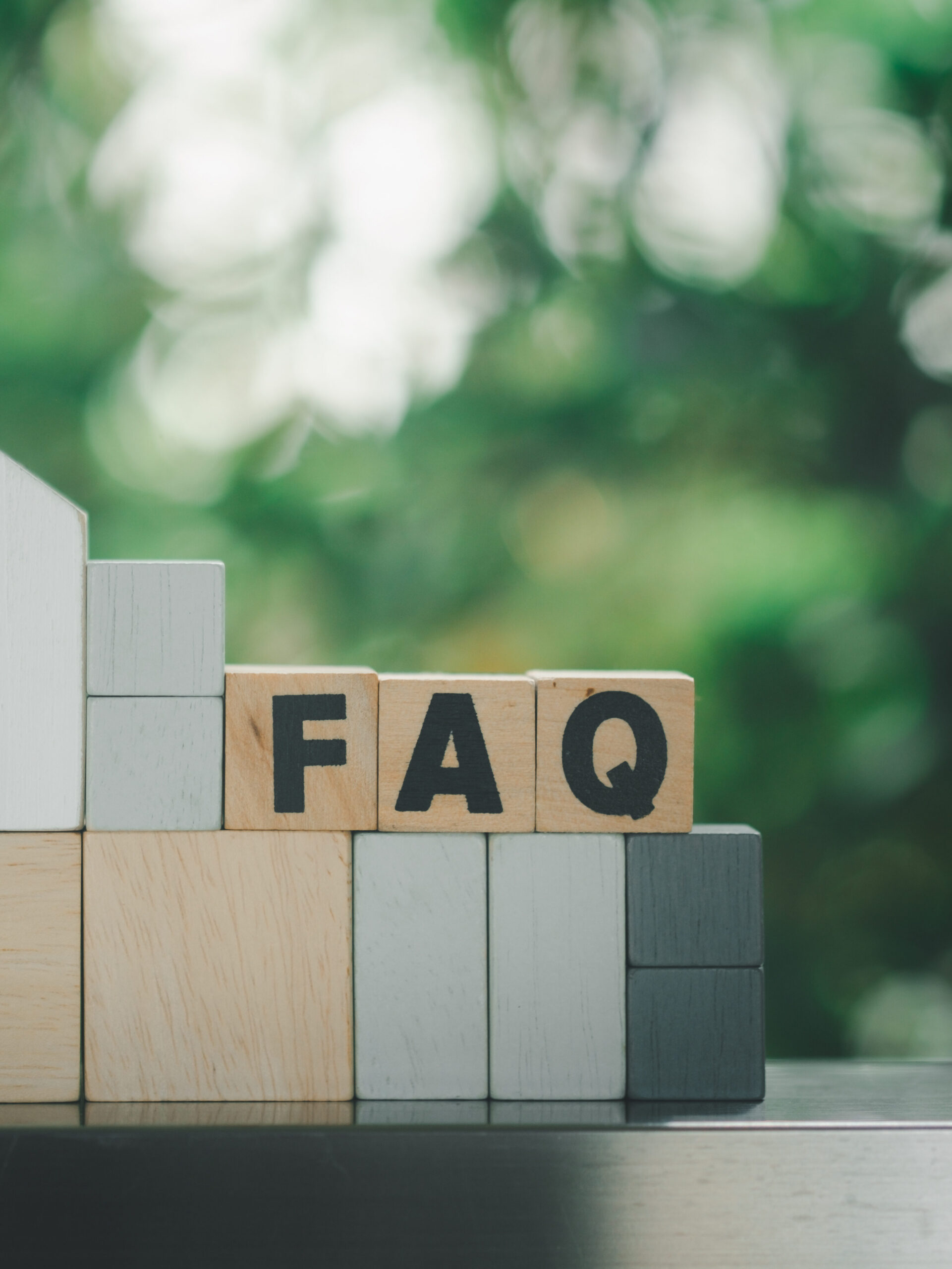Wooden blocks arranged in a staircase pattern, with three central blocks featuring the letters "F," "A," and "Q." The background is green and blurred, suggesting an outdoor setting.